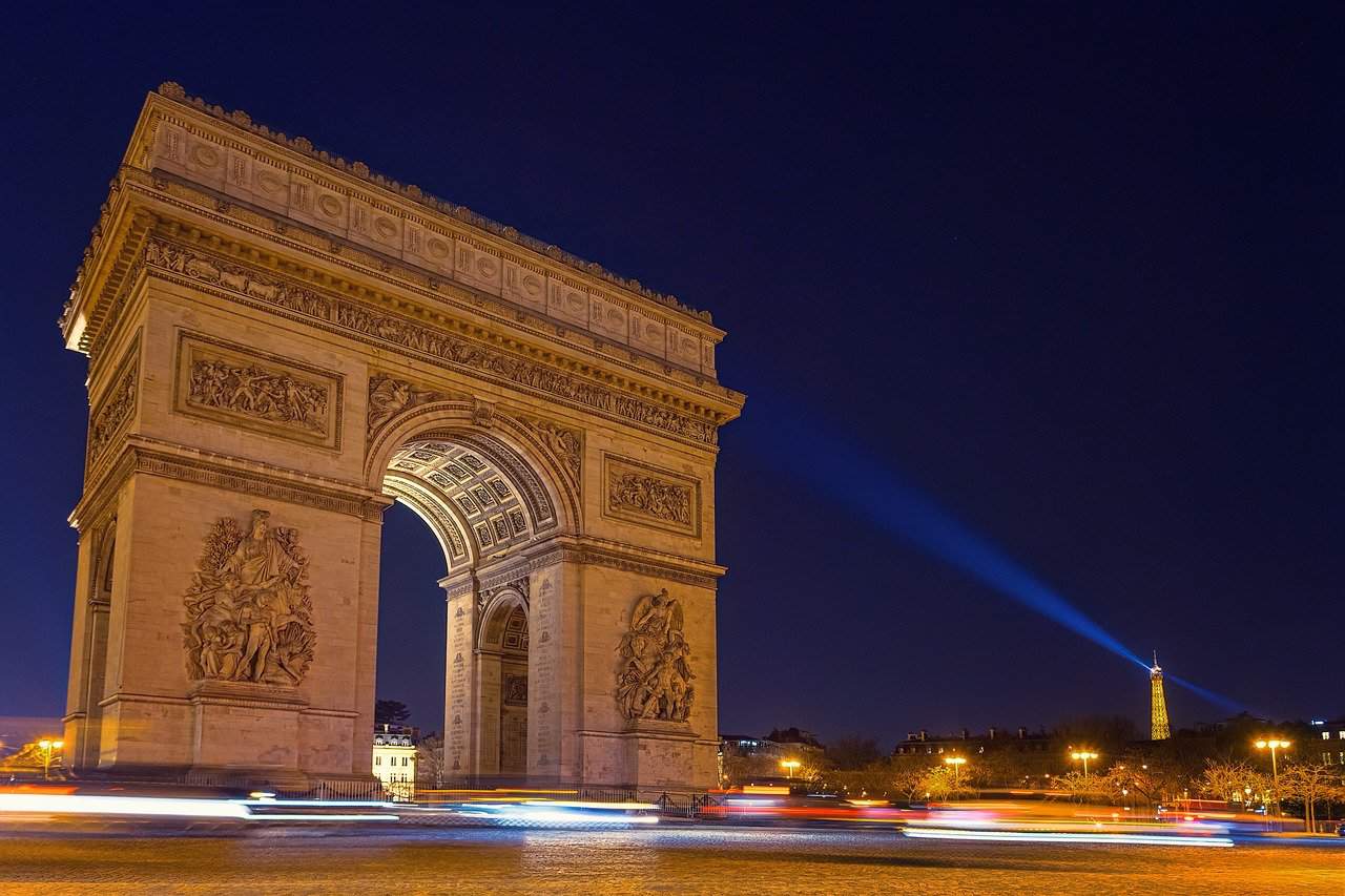 The Arc de Triomphe at night in Paris with the Eiffel Tower light glowing towards it