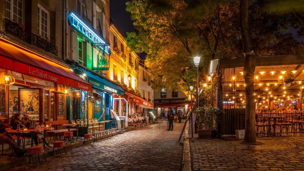 Quiet Parisian street with colorful lit signs outside of some empty businesses