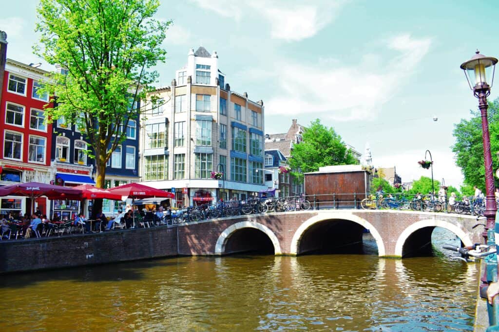 Large bridge crossing a canal in Amsterdam with many people walking over it and enjoying a cafe on the corner
