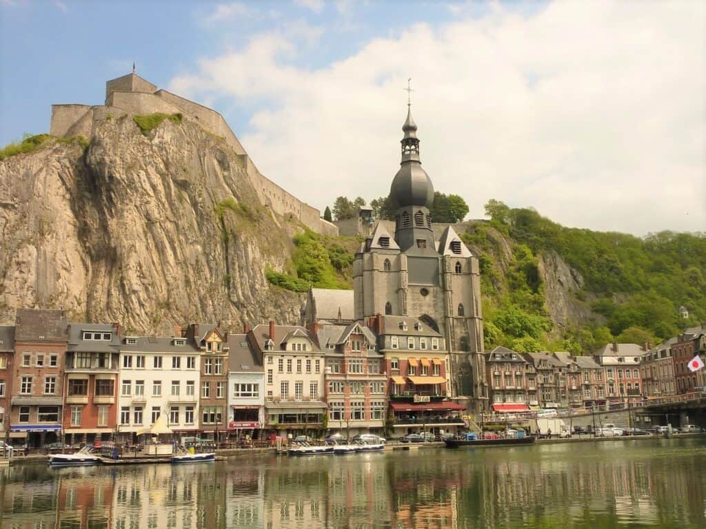 Dinant, Belgium's line-up of colorful buildings and tall church backed by a rocky mountain on a river