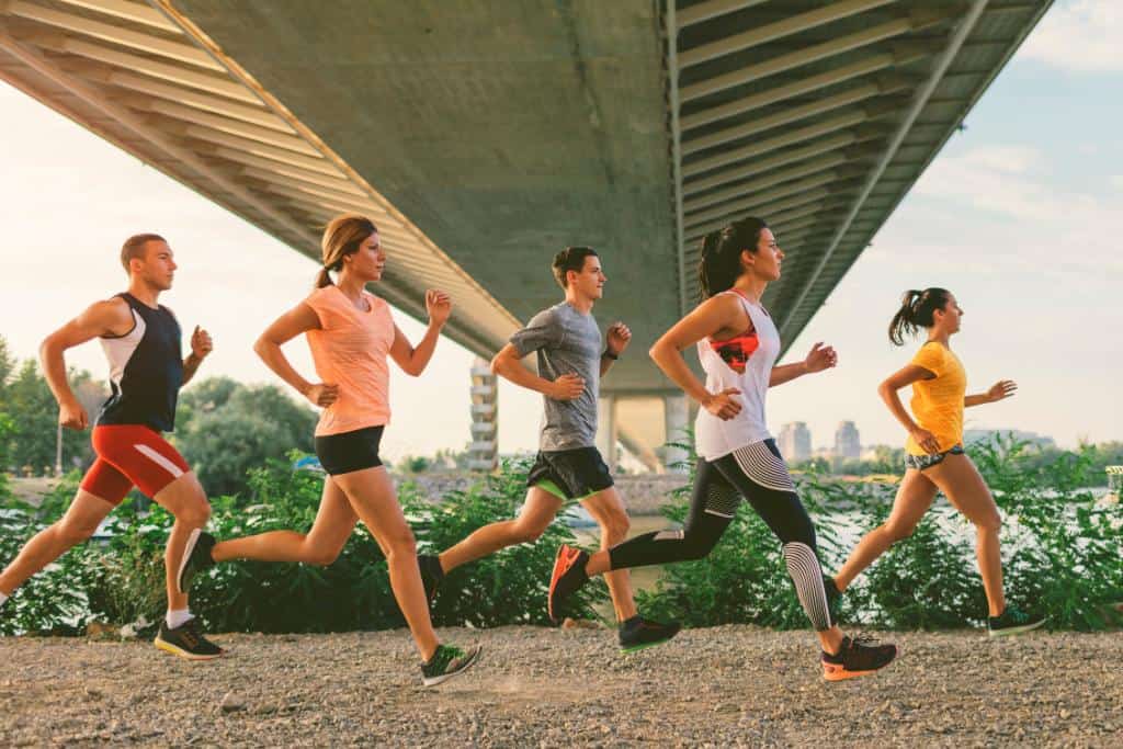 5 people running under a bridge in athletic gear