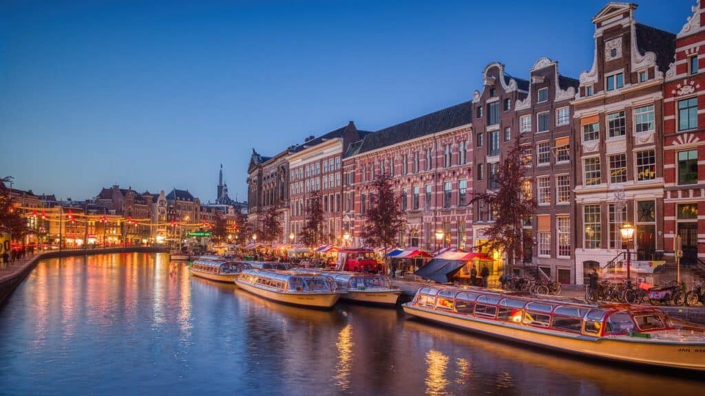 Canal in Amsterdam covered in golden lights from the boats and restaurants