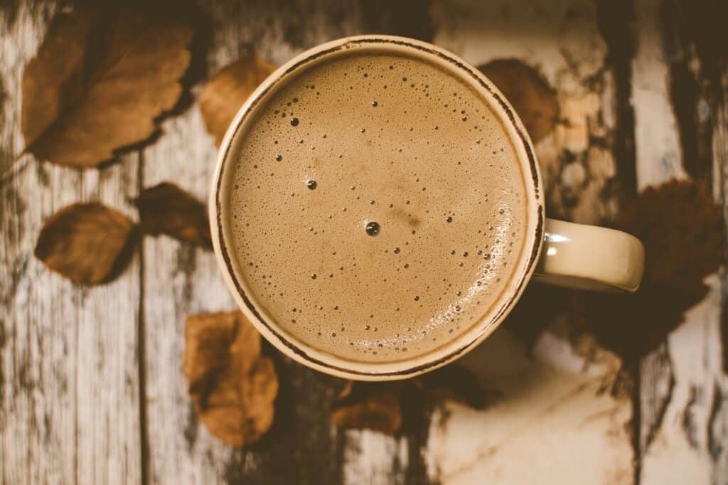 A coffee mug with coffee surrounded by leaves on a wooden table