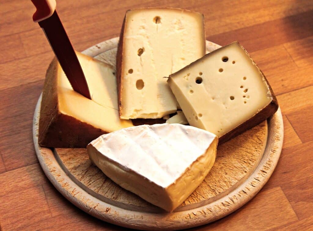 Wooden circular board with 4 triangles of cheese and a knife sticking out of one of them
