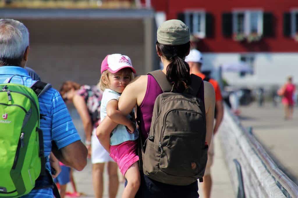 Woman with a backpack carrying a child; both are wearing baseball hats