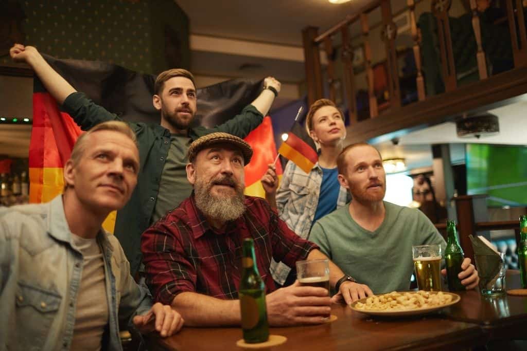 Group of people watching a game with beers and holding German flags