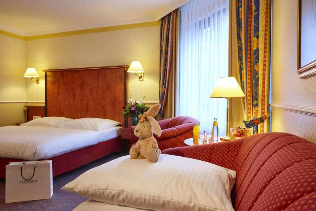 Hotel room with a red couch, pillows, and a stuffed animal