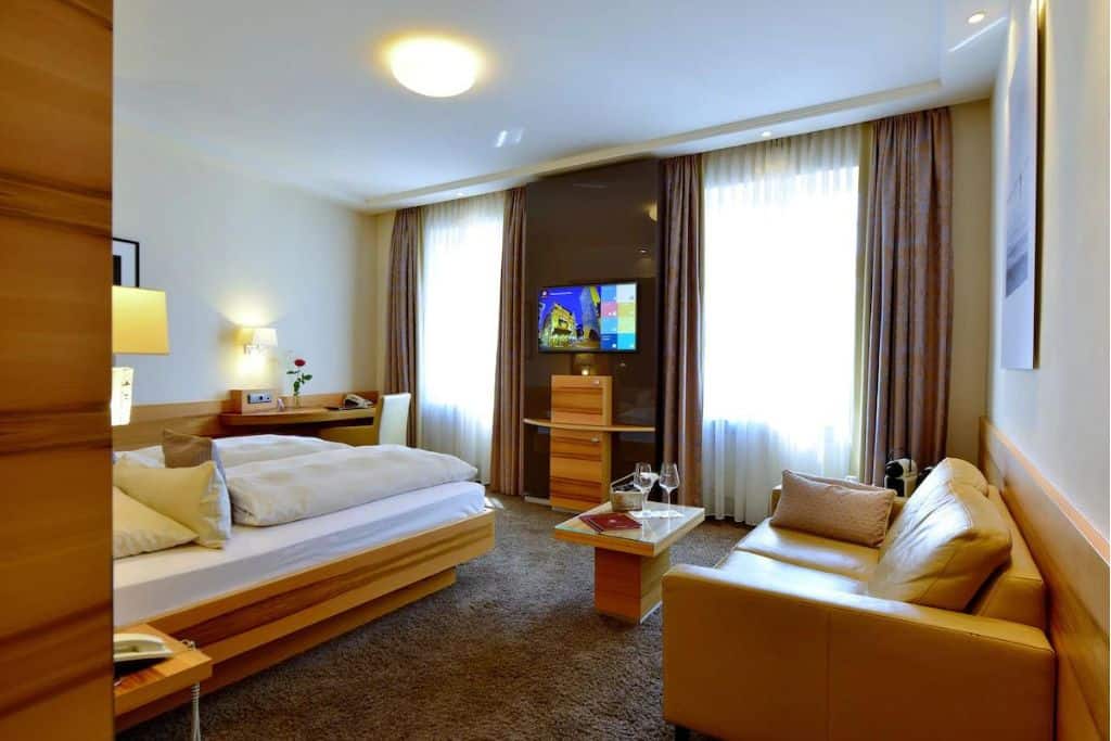 Modern hotel room with a bed, couch, and coffee table with wine glasses