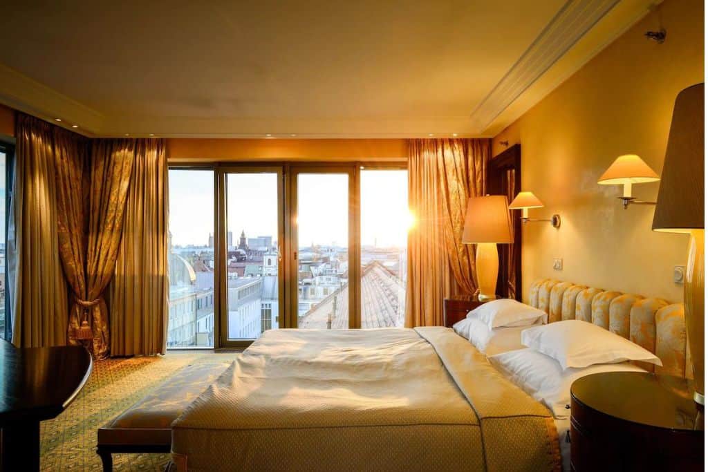 Large hotel room with tall windows overlooking Munich at sunrise