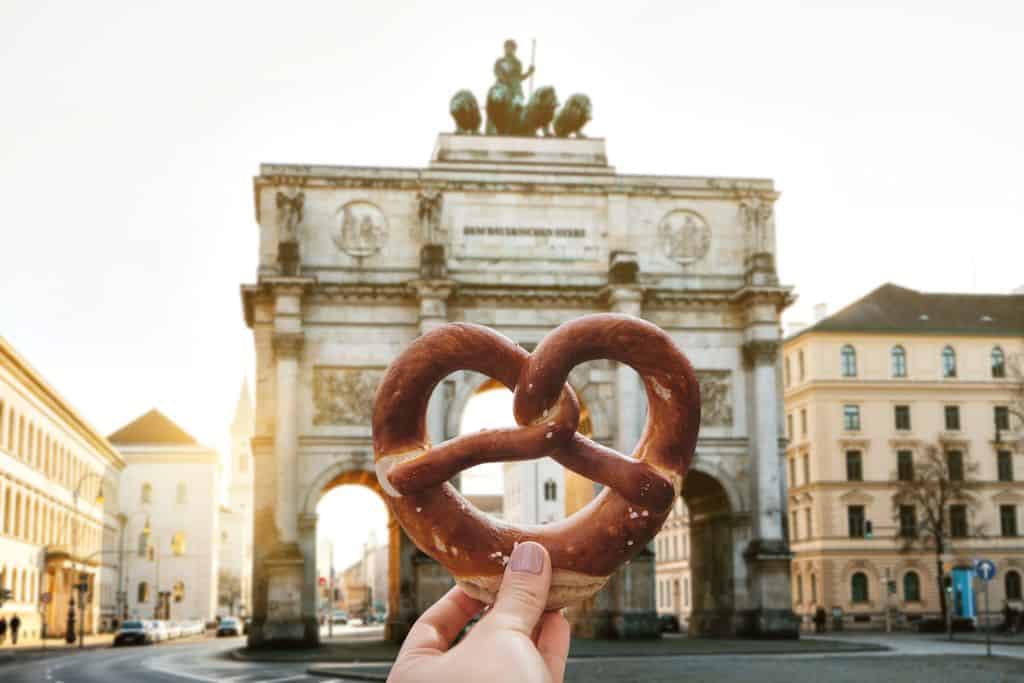Hand holding a German pretzel in front of Berlin's Brandenburg Gate