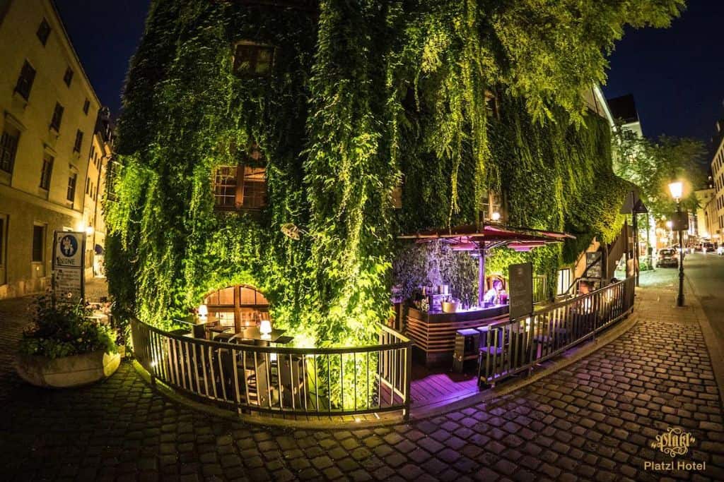 Illuminated hotel with green trees and pretty lights over a cobblestone street at night