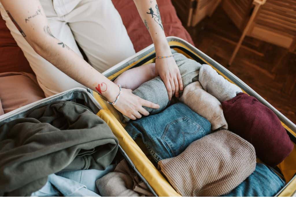Person with arm tattoos packing a suitcase full of warm clothing