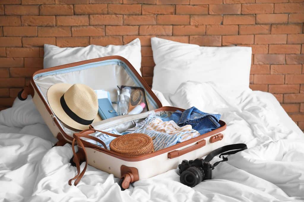 White and brown suitcase filled with summer clothes on a bed