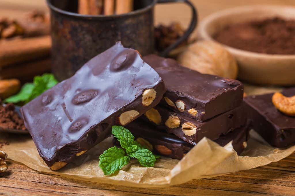 Bars of chocolate with nuts on a wooden board with parchment paper and mint leaves