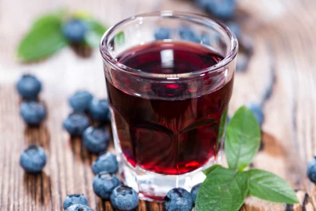 Glass of Hungarian Pálinka surrounded by blueberries and mint leaves