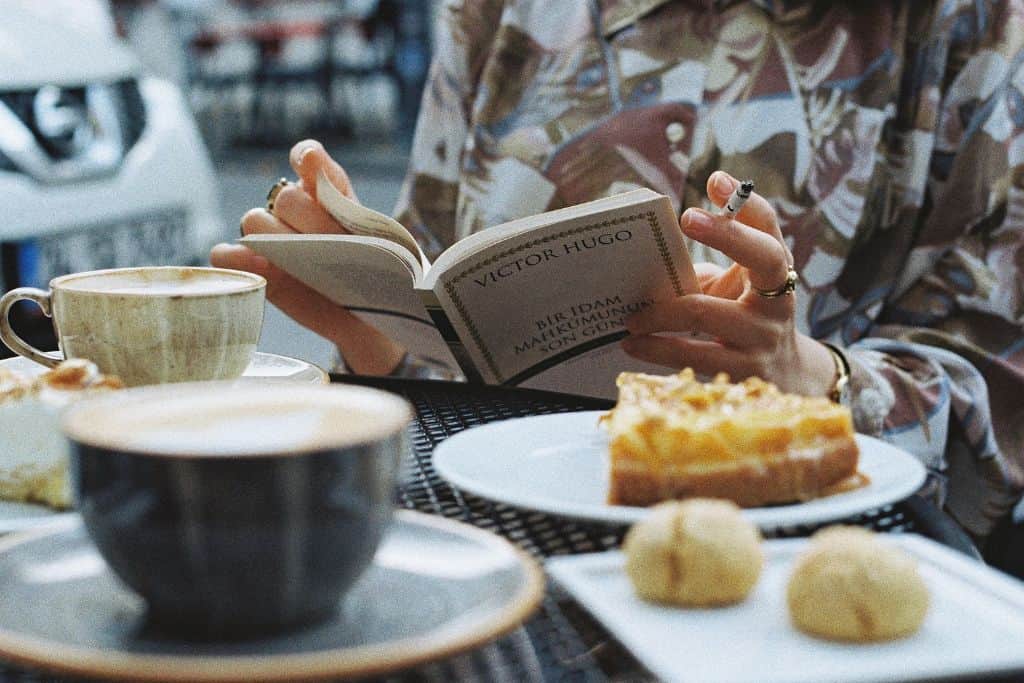 Someone reading a book at a breakfast table with coffee and sweet treats