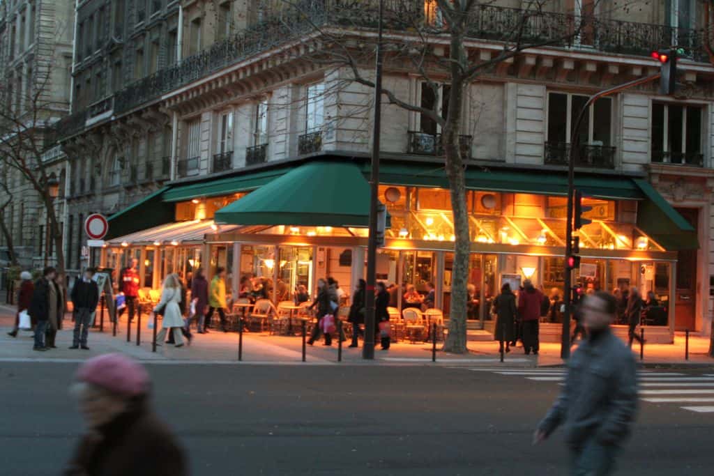 Busy street around a golden lit restaurant in Paris