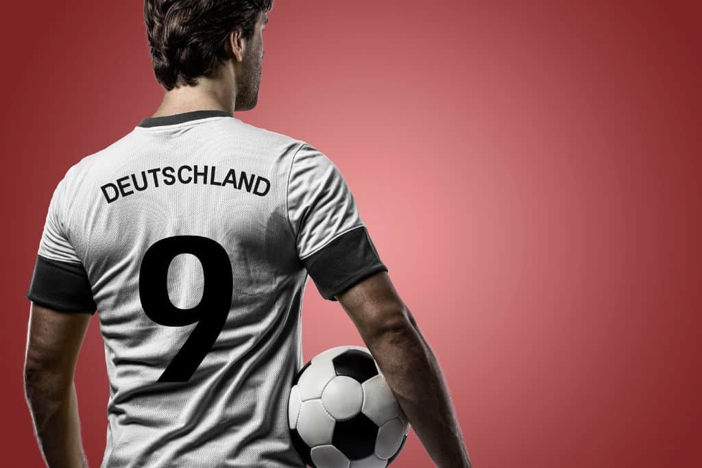 Male soccer player holding a ball and wearing a jersey that says the #9 and "Deutschland"