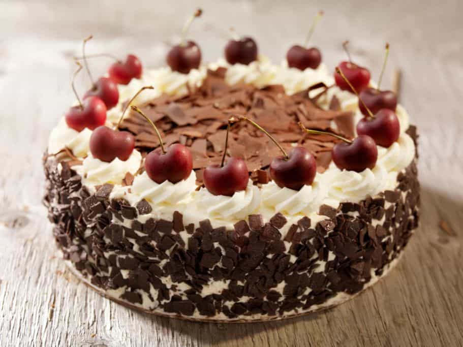 An uncut black forest cake with cherries on top