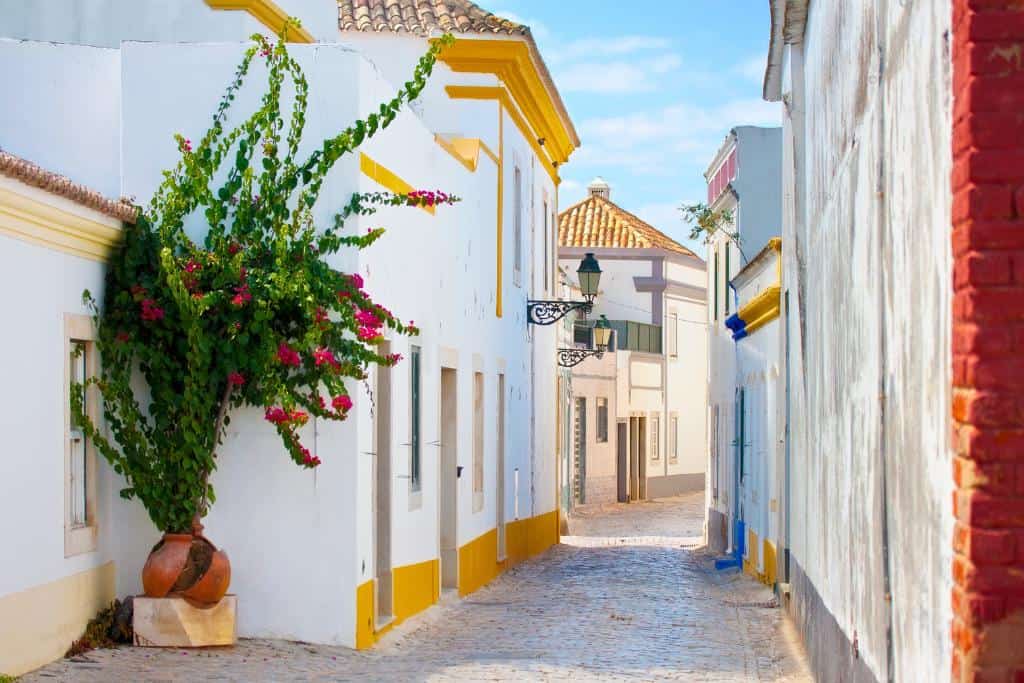 Narrow cobblestone street with white homes and yellow trim in southern Portugal