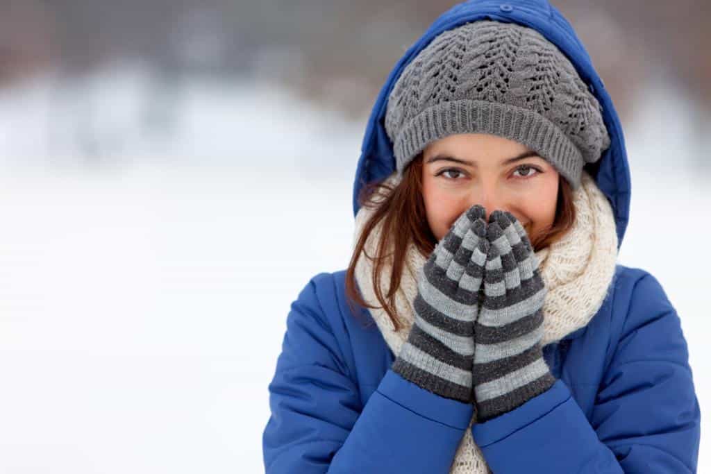 Girl in a blue jacket, white scarf, striped mittens, and a knit hat in the snow