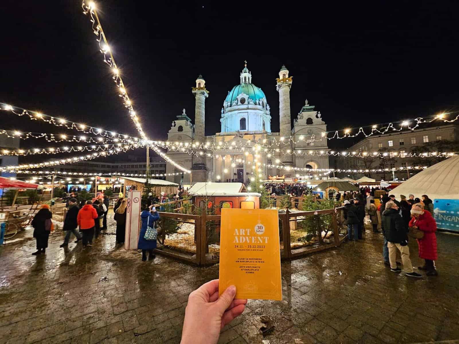 Hand holding an "Art Advent" calendar in from of Vienna's Christmas Market