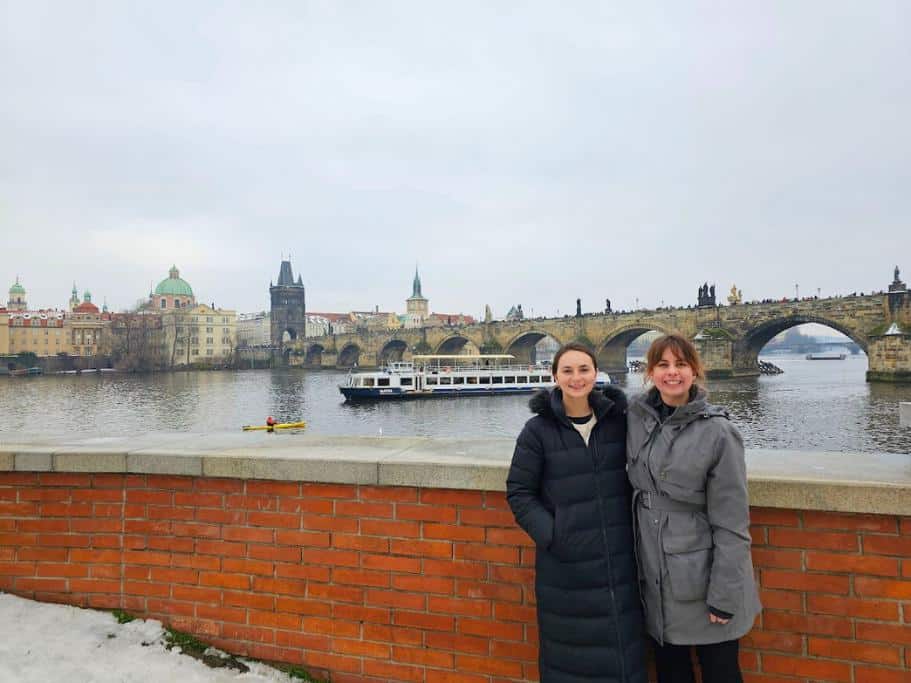 Two girls smiling in front of the Charles Bridge in Prague in winter