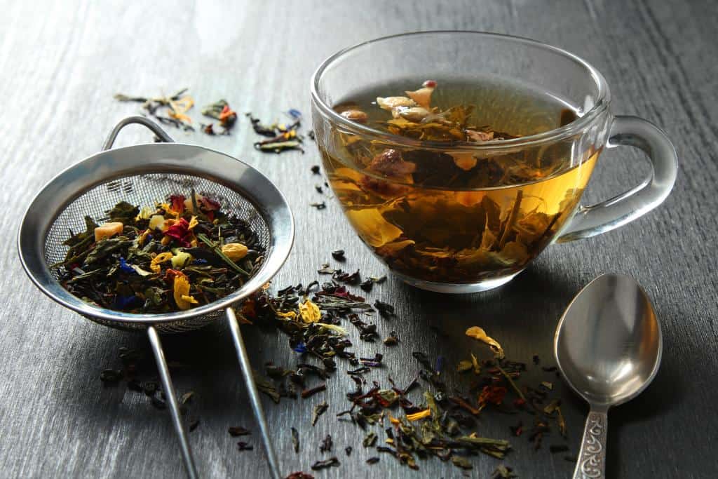 Glass mug of tea next to a loose tea strainer and a silver spoon