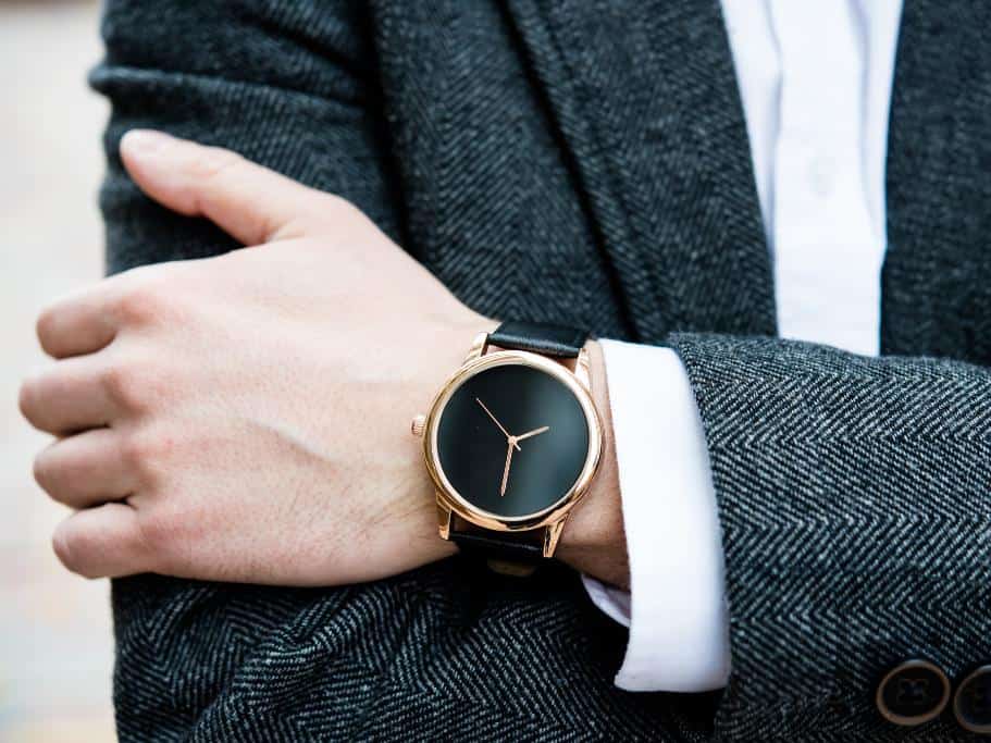 Man's black and gold watch against a charcoal suit