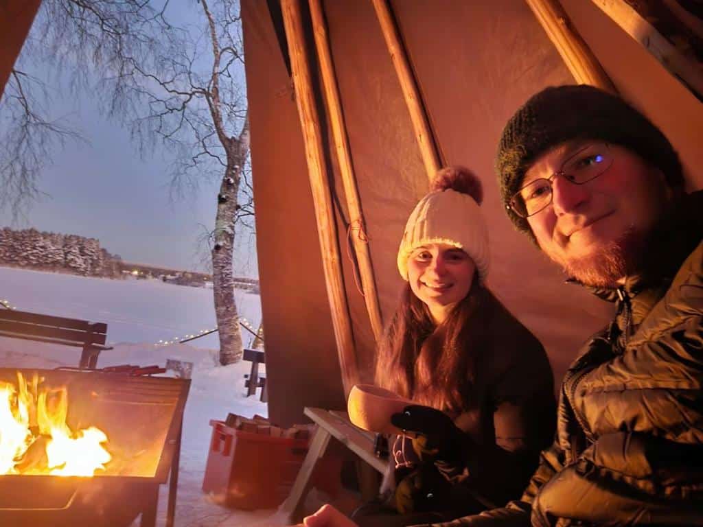 Two people sitting in a traditional Finnish hut with a fire in Rovaniemi, Finland