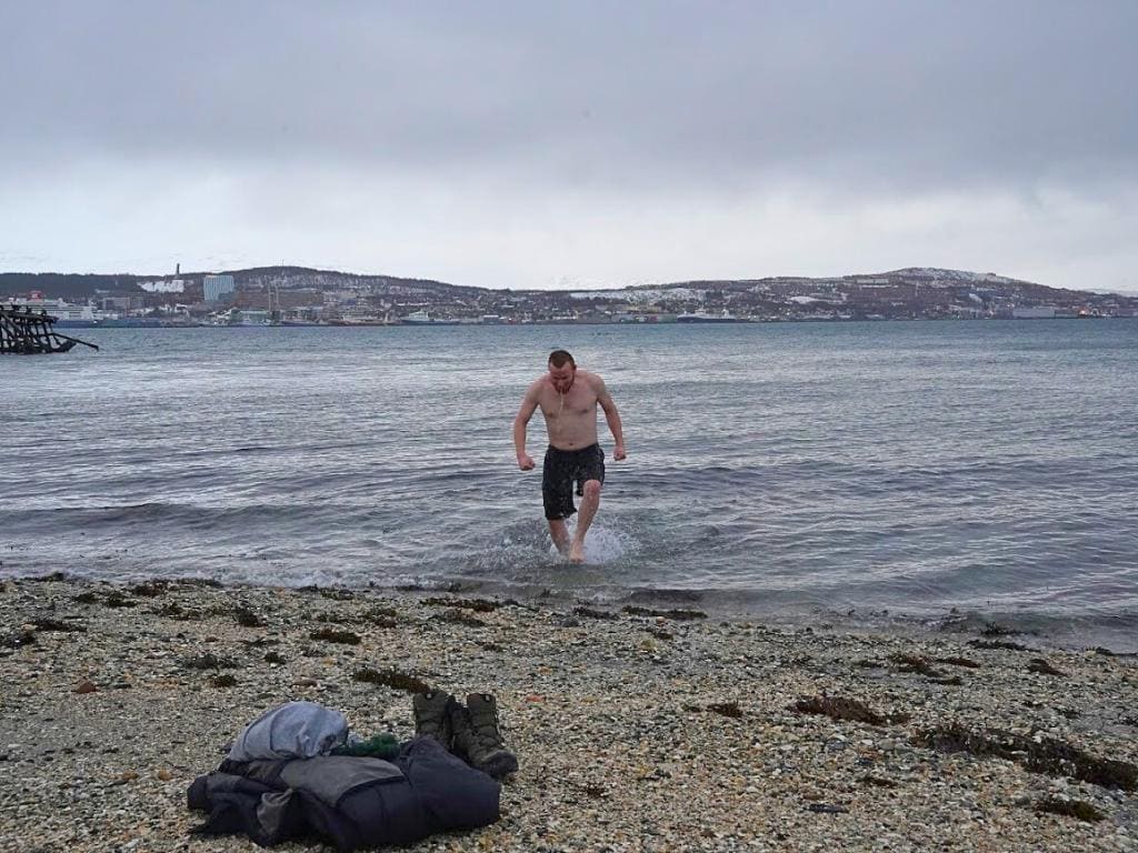 Man in a bathing suit running out of the ocean on a small beach in Tromso, Norway