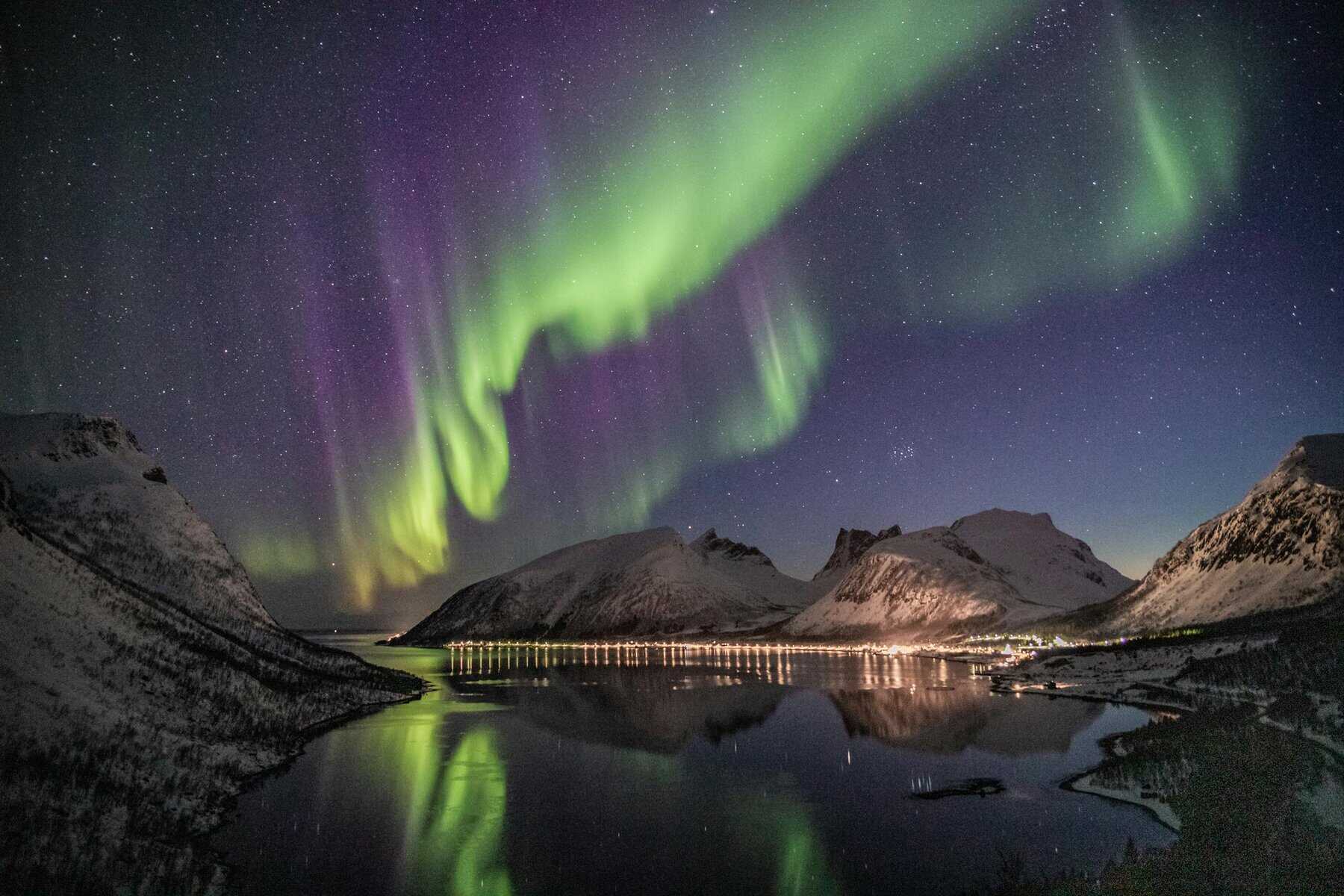 Beautiful aurora borealis over a snow-capped mountain lake at night with stunning reflections.