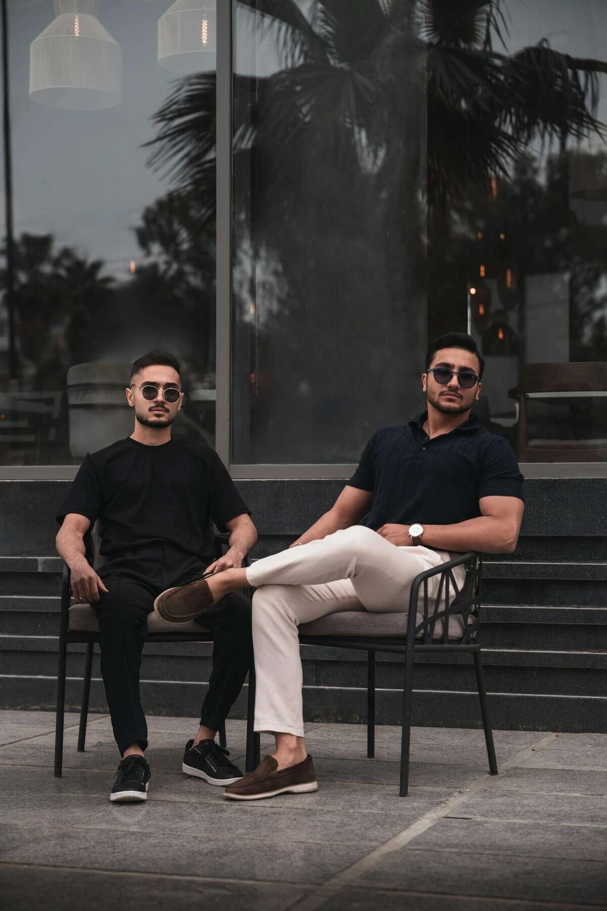 Two well-dressed men in sunglasses sitting at an outdoor cafe table