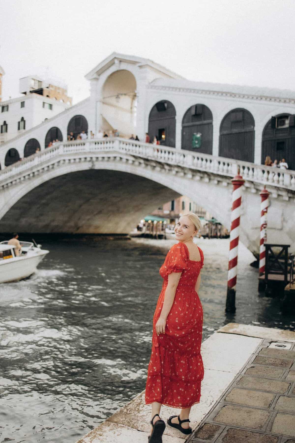 A woman in a red dress enjoying a scenic view by the historic Rialto Bridge in Venice, Italy.