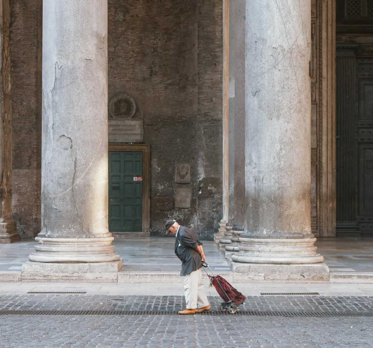 Elderly man with suitcase walking past large columns in Rome. Urban scene in Italy.